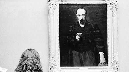 Frau betrachtet ein gerahmtes Porträt in einem Museum und achtet auf Blick, Mimik und Gesichtsausdruck der dargestellten Figur.