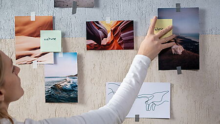 Frau ordnet verschiedene Fotografien und eine Linienzeichnung an einer Inspirationswand.