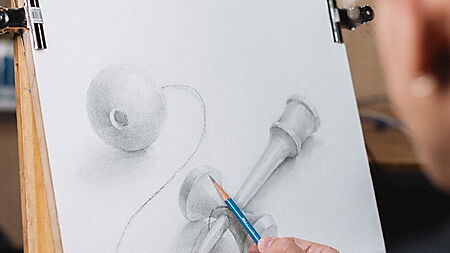 Ein Zeichner skizziert ein Kendama und baut das Motiv sichtbar aus Kugel, Zylinder und geschwungenen Linien auf.