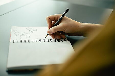 Hand zeichnet mit Bleistift abstrakte Linien in ein Skizzenbuch und zeigt einen freien, suchenden Zeichenmoment.