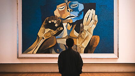 Mann steht in einer Galerie vor einem abstrakten Gemälde und nähert sich dem unbekannten Werk durch ruhiges Betrachten.