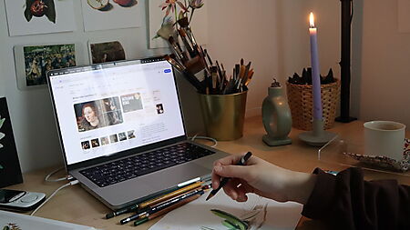 Kreativer Arbeitsplatz mit Laptop, Zeichenmaterial und floralen Skizzen zeigt, wie Online-Angebote beim Zeichnenlernen inspirieren können.