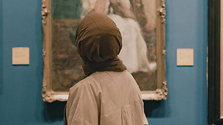 Frau betrachtet ein gerahmtes Gemälde in einer Kunstgalerie und nimmt Details, Aufbau und Wirkung des Bildes bewusst wahr.