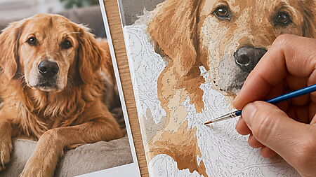 Hand malt mit einem feinen Detailpinsel an einer personalisierten Malen-nach-Zahlen-Leinwand eines Hundes; daneben liegt das Originalfoto.