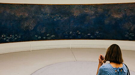 Frau im blauen Kleid, auf einem weichen Hocker sittzend, betrachtet allein die die Nymphéas von Claude Monet, mehrere großformatige Landschaftsbilder, im "Musée de l'Orangerie" in Paris.