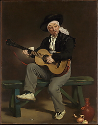 Ein sitzender Mann in spanisch anmutender Kleidung spielt Gitarre vor einem dunklen Hintergrund.